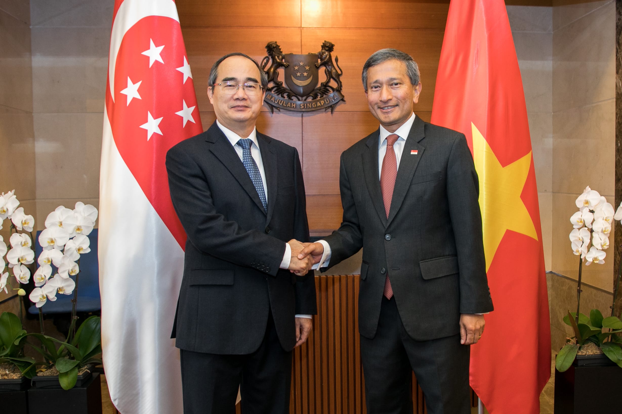 Two men in suits shake hands before Singapore and Vietnam flags.